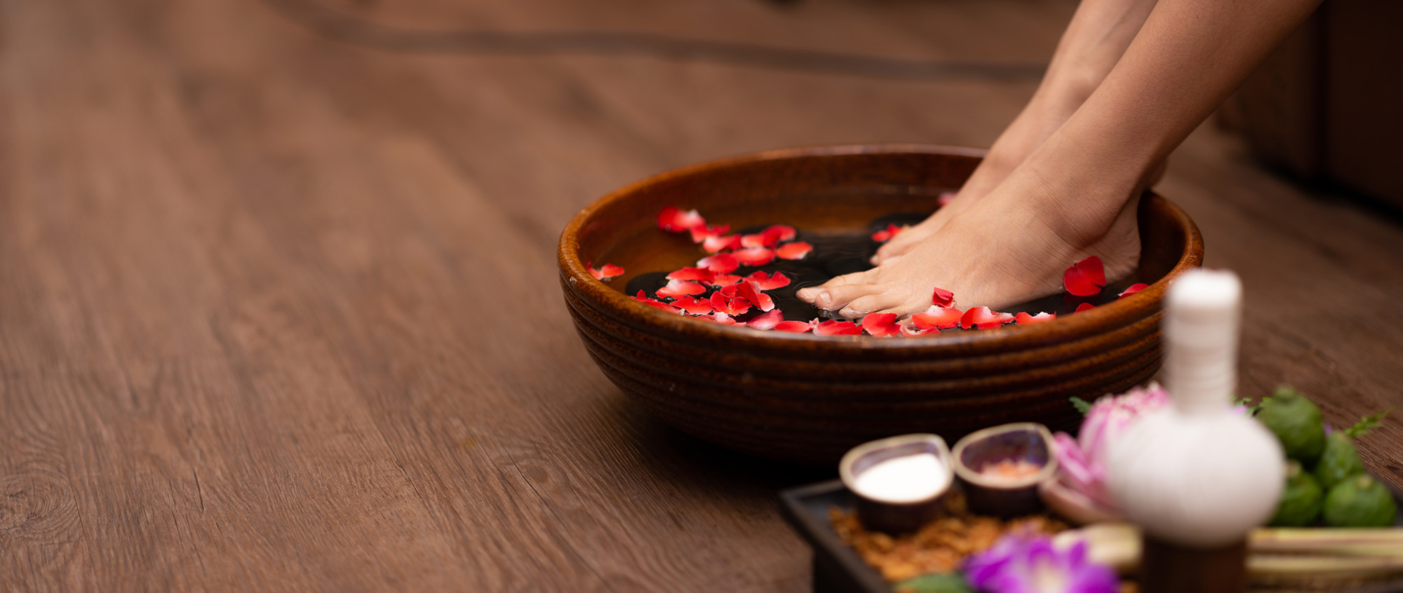 Closeup shot of a woman feet dipped in water with petals in a wooden bowl. Beautiful female feet at spa salon on pedicure procedure. Bain de pied salon de massage bien-être